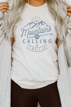 Introducing our "The Mountains Calling And I Must Go" Graphic Tee, a perfect choice for adventure enthusiasts and outdoor lovers. Most t shirt colors are 52/48 cotton/poly blend. White and Cream tees are 100% cotton, Ash tees are 99/1 cotton/poly. Available in various sizes, it's an excellent addition to outdoor retail stores and adventure-themed boutiques. Encourage your customers to answer the call of the mountains with our "The Mountains Calling And I Must Go" Graphic Tee. By Kissed Apparel.M Blue T-shirt With Letter Print For Outdoor, White Pre-shrunk T-shirt For Hiking, Blue Graphic Tee For Outdoor Activities, Blue Cotton T-shirt For Outdoor Activities, White Pre-shrunk Tops For Outdoor Activities, Blue Cotton Tops For Camping, White T-shirt With Text Print For Outdoor Activities, Outdoor Blue T-shirt With Letter Print, Graphic Tee With Text Print For Outdoor Activities