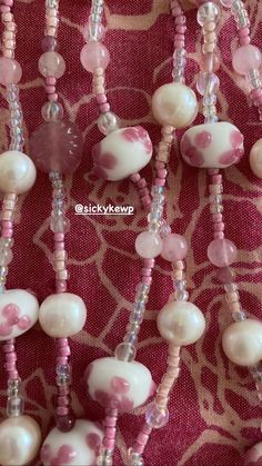 pink and white beaded necklaces are displayed on a red fabric with an intricate design