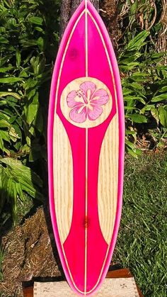 a pink surfboard sitting on top of a wooden table next to a tree and grass