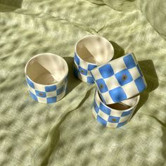 three blue and white checkered cups sitting on top of a bed