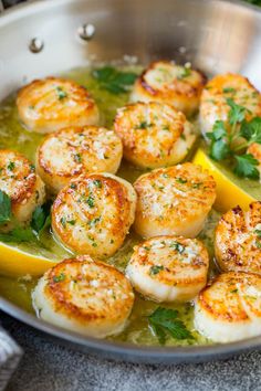 some scallops are cooking in a pan with lemon wedges and parsley