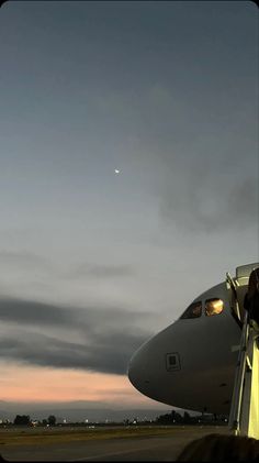 an airplane sitting on top of an airport tarmac at dusk with the moon in the distance