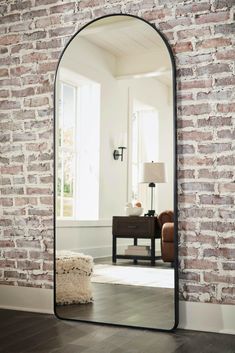 a large black mirror sitting on top of a wooden floor next to a brick wall