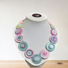 a necklace is displayed on a white mannequin with pink, blue and green buttons