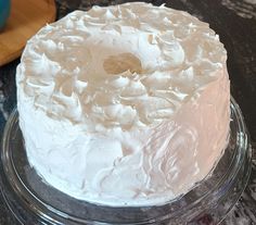 a cake with white frosting sitting on top of a glass plate next to a wooden cutting board