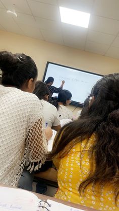 several people sitting at a table in front of a projector screen with writing on it