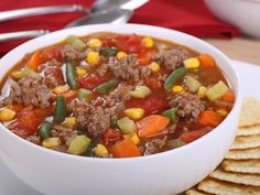 a white bowl filled with meat and vegetable soup next to crackers on a plate