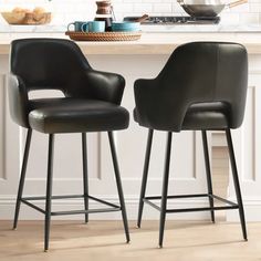 two black leather bar stools sitting in front of a kitchen counter with white cabinets