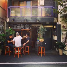 three men sitting at an outdoor bar in front of a building with lots of plants