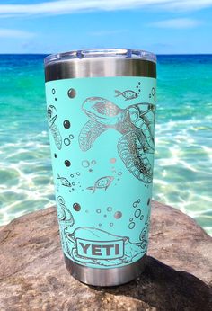 a blue yeti cup sitting on top of a rock near the ocean with an image of a sea turtle