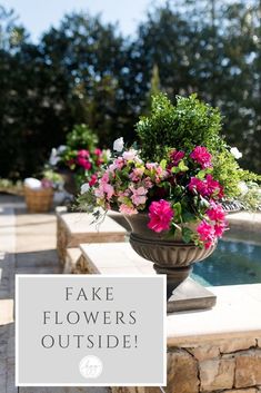 fake flowers outside in a vase sitting on a stone wall with the words fake flowers outside