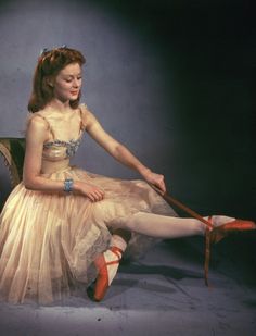 a woman in a dress sitting on a chair with her legs crossed and wearing red shoes