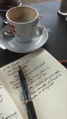 a pen sitting on top of an open notebook next to a coffee cup and saucer