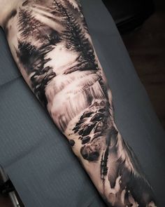 a man's arm covered in black and white ink with trees on the side