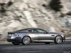 a silver sports car driving down a road next to a rocky mountain side with its hood up