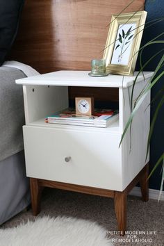 a nightstand with a clock on top of it next to a plant and a bed