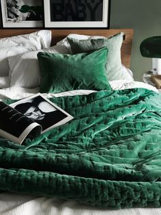 a bed with green sheets and pillows in a bedroom next to two framed pictures on the wall