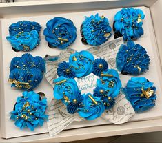 twelve blue cupcakes in a white box with gold decorations