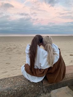 two women sitting on a wall looking out at the ocean