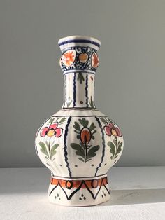 a white and orange vase sitting on top of a table next to a gray wall