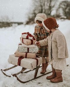 two children pulling a sleigh with presents on it in the snow and one child is wearing a hat