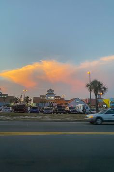 cars are driving down the road in front of some buildings and palm trees at sunset