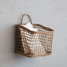 a woven basket hanging on the wall holding two white tissues and a brown paper bag