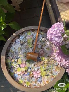 a bucket filled with lots of flowers next to a purple flower pot and a broom