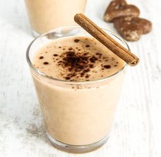 two glasses filled with milk and cinnamon on top of a white table next to cookies