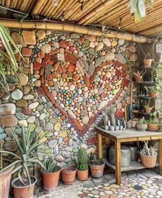 there is a heart made out of rocks on the side of a wall with succulents and potted plants