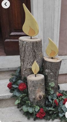 three wooden logs with candles on top of them sitting in front of a wreath and door