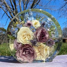 a glass vase filled with flowers sitting on top of a wooden table next to a tree