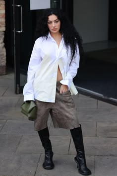 a woman with long black hair is standing on the sidewalk