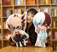 two anime pillows sitting on top of a table next to a woman holding an item