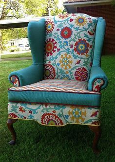 an upholstered chair sitting in the grass with blue and red fabric on it