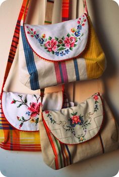 three purses are hanging on the wall with different colors and designs, one is white