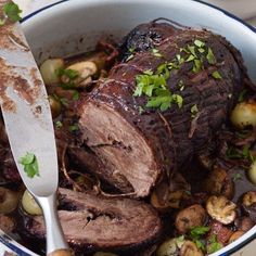 a roast beef with mushrooms and parsley in a white bowl next to a knife