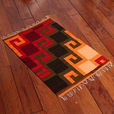 a colorful rug on the floor with fringes around it and an orange, black, green, red, yellow, and brown color scheme