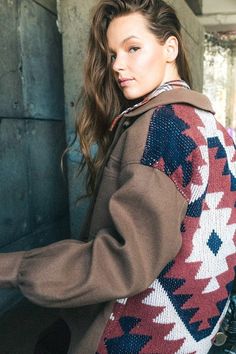 a woman leaning against a wall wearing a sweater