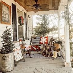 the porch is decorated for christmas with plaid blankets and pillows on it, as well as potted trees