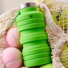 a green water bottle sitting next to tennis balls on top of a netted bag