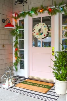 a pink front door decorated with christmas garland and lights