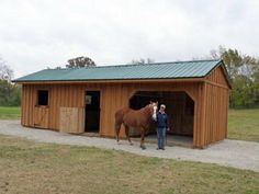 a woman standing next to a brown horse in a wooden shed with a green roof