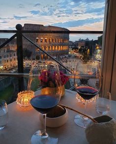 two wine glasses sitting on top of a table next to a window with the city in the background