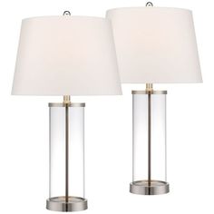 two clear glass lamps with white shades on them