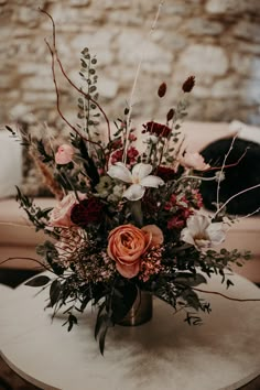 an arrangement of flowers on a table in front of a brick wall with a sofa