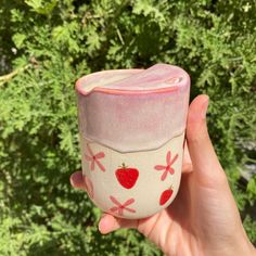 a hand holding a cup with strawberries painted on the outside and pink paint on the inside