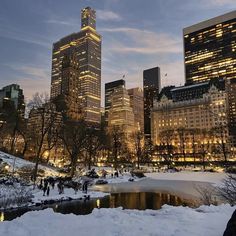 the city skyline is lit up at night with snow on the ground and people walking around