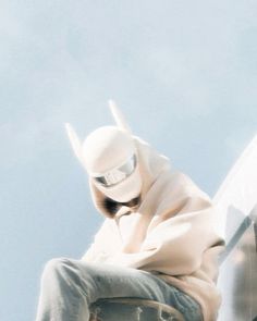 a man sitting on the side of a building while wearing a white mask and jacket