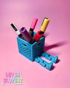 a blue basket filled with lots of different types of pens and pencils on top of a pink background